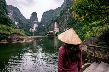 Trang Bir Manzara karst kuleleri ve nehir (Unesco Dünya Mirası) boyunca bitkiler tarafından oluşturulan bir Manzara hasır şapka ile Vietnamlı Kız. Vietnam topraklarındaki Halong Körfezi. Ninh Binh province, Vietnam.