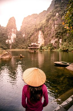 Trang Bir Manzara karst kuleleri ve nehir (Unesco Dünya Mirası) boyunca bitkiler tarafından oluşturulan bir Manzara hasır şapka ile Vietnamlı Kız. Vietnam topraklarındaki Halong Körfezi. Ninh Binh province, Vietnam.
