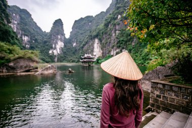Trang Bir Manzara karst kuleleri ve nehir (Unesco Dünya Mirası) boyunca bitkiler tarafından oluşturulan bir Manzara hasır şapka ile Vietnamlı Kız. Vietnam topraklarındaki Halong Körfezi. Ninh Binh province, Vietnam.