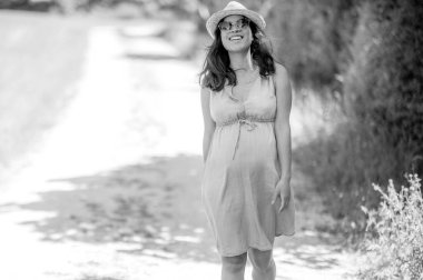 Güneş gözlüklü ve şapkalı mutlu hamile kadının açık havada portresi - doğada yaz zamanı - aile hayatının güzel anları