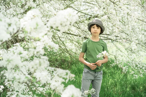 シャツと帽子立っている花盛りの木を背景に少年のポートレート — ストック写真