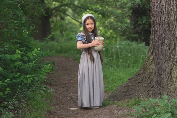 穿着复古风格衣服的女孩在森林里拿着一个陶土壶 — 图库照片