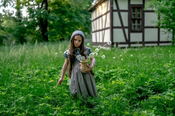 女孩在复古风格的礼服与白色蒲公英和粘土锅在典型的建筑和建筑的老德国 木材框架 — 图库照片