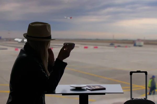 Cup of coffee at the airport.Young woman is drinking coffee in airport.Airline passenger in an airport lounge drinking coffee and waiting for flight aircraft. Caucasian woman with glass if hot coffee.