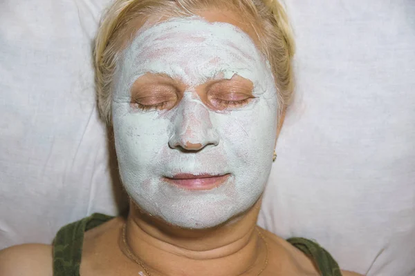 Aged woman with a cosmetic mask on face at home - beauty treatments concept.