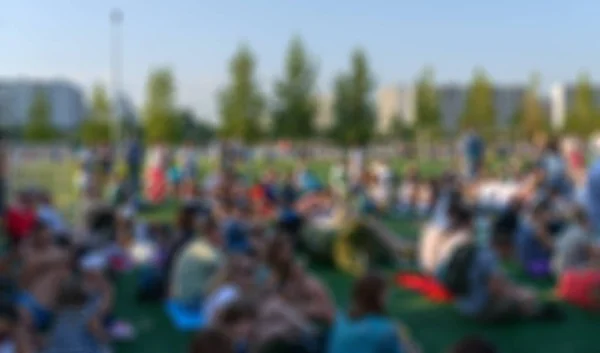 Blurred group of people sitting on grass.