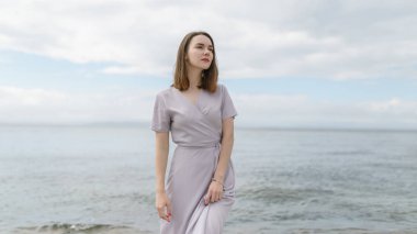 Elbiseli kadın deniz kıyısında yürümekten hoşlanıyor..