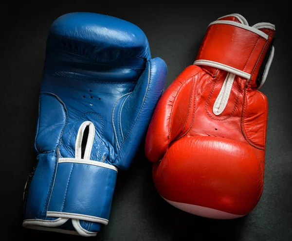 Old and used boxing gloves on dark background.