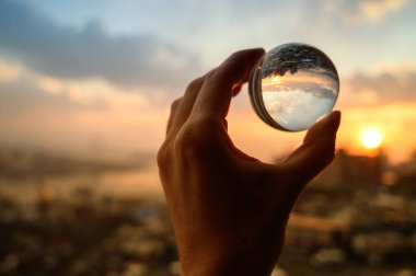 El şehir üzerinde gün batımı gökyüzü yansıtan cam topu tutar.