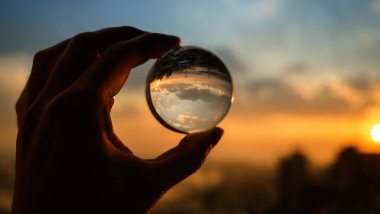 El şehir üzerinde gün batımı gökyüzü yansıtan cam topu tutar.