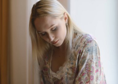 Pencere nin üzerinde oturan bornozla travesti kadın. Doğal ışık.