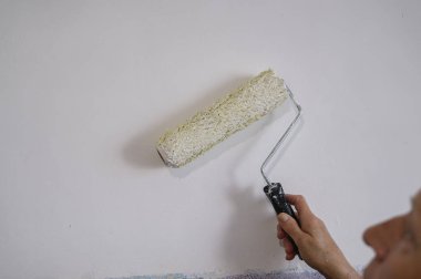 İç duvarı beyaz boyayla boyayan yaşlı bir kadının otantik fotoğrafı..