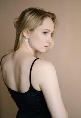 Siyah bluzlu zarif genç kadın bej duvara karşı poz veriyor..