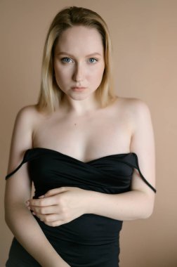 Siyah bluzlu zarif genç kadın bej duvara karşı poz veriyor..