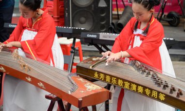 MISHAN, CHINA - JULY 28, 2019: Children dressed in the Chinese traditional costume plays Chinese musical instrument - Gu Zheng. Mishan is a county-level city in the southeast of Heilongjiang Province. clipart