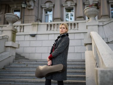 Palto giymiş güzel bir kız, elinde eski bir keman çantası var..