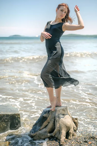 身穿黑色衣服的年轻女子坐在沙滩上欣赏大海 — 图库照片