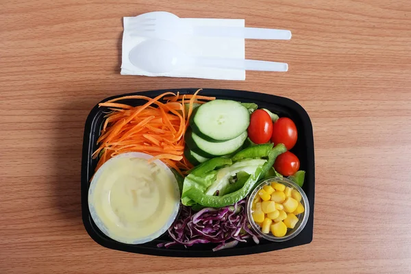 Taze karışımı salata ve şeffaf plastik kutusu pansuman. domates, havuç dilimleri, mor lahana dilimlenmiş, dilimlenmiş salatalık ve mısır çekirdekleri ahşap zemin üzerinde. Yemeye hazır. Üstten görünüm