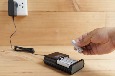 Ahşap masa üzerinde şarj cihazı ile şarj edilebilir pil boyutu Aa tutan el