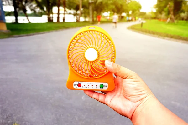 Hand holding portable fan at the public park in summer, hot weather