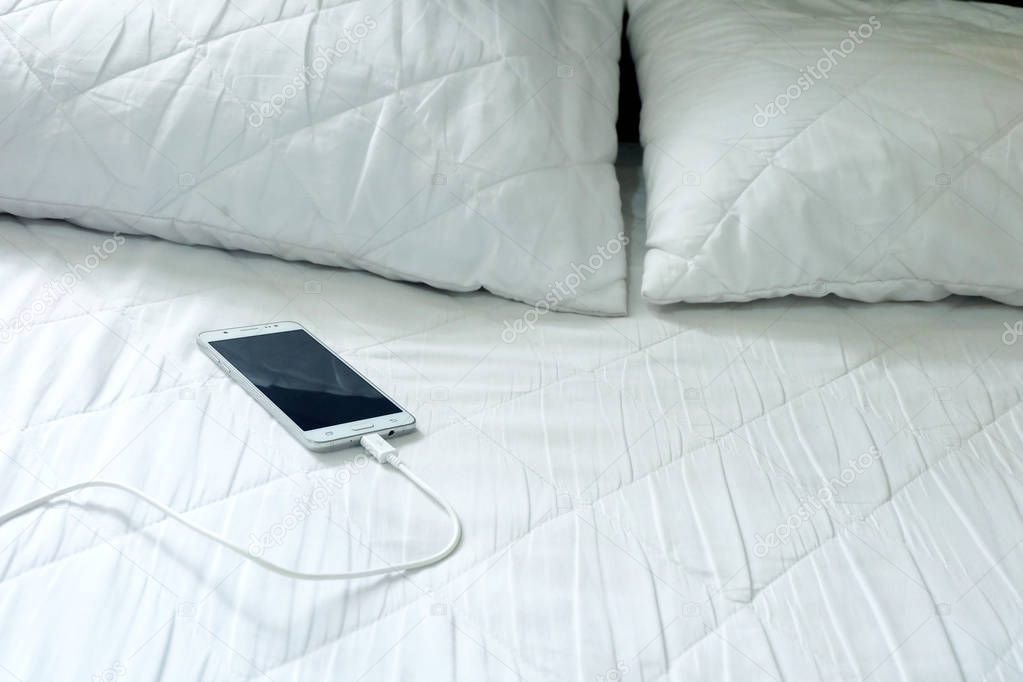 Smart phone is charging on the white bed
