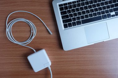 Adaptör güç kablosu şarj dizüstü bilgisayarın üzerinde ahşap bir masa, üstten görünüm