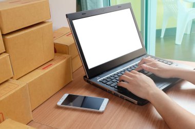 Kadın yazarak dizüstü bilgisayar, cep telefonu ve ürün Online alışveriş, kutusu, ahşap zemin üzerinde iş evde, e ticaret