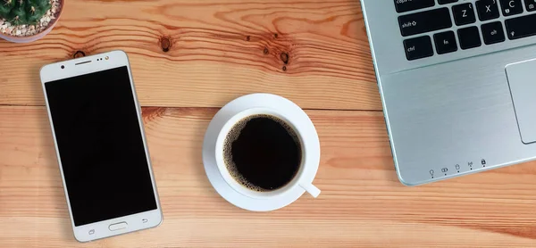 Black coffee in white cup and laptop computer and Mobile Phone or Smartphone with blank screen on wooden floor, Horizontal photo banner for website header design Top view, copy space