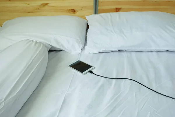 Smart phone is charging is plugged on the white bed, The danger of charging electricity when sleeping