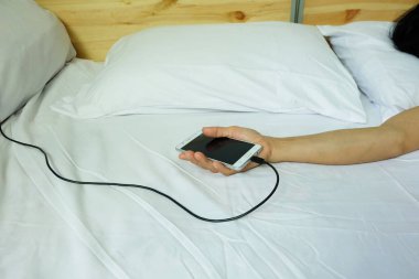 El kullanımı akıllı telefonlar tutuyor. şarj cihazı beyaz yatakta takılı, uyurken elektrik şarj tehlikesi