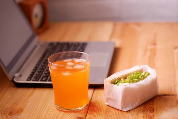 Eat sandwich and orange juice. During work with laptop computer. Work and eat food at the same time. Work at home.