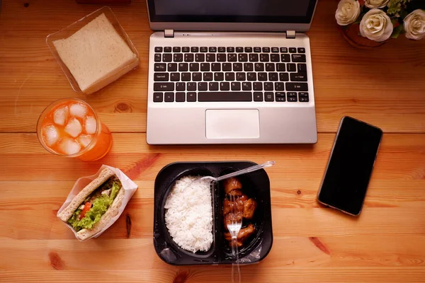 Eat sandwich and Meal plastic box with orange juice. During work with laptop computer. Work and eat food at the same time. Work at home.