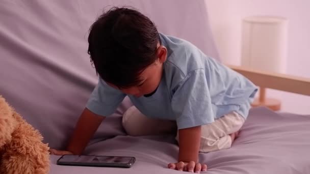 2 yaşında tatlı bir Asyalı. Oturma odasındaki kanepede oturup cep telefonu izleyip oynuyor.. — Stok video