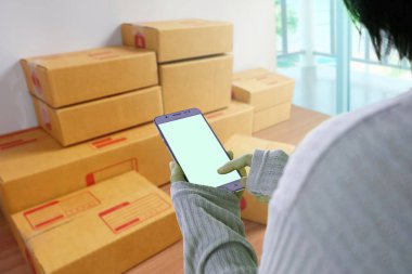 Akıllı telefondan sipariş alan ve ürünü kutuya, online iş sahiplerine veya online alışveriş konseptine koymaya hazırlanan Asyalı genç bir kadın.