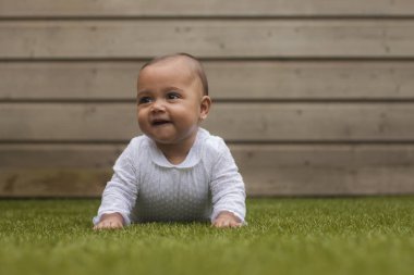Gülümseyen ve göbek beyaz giyim suni çim üzerinde yatan bir altı aylık şirin bebek kız portresi