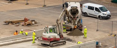 Southampton limanı, İngiltere, İngiltere - 08 Haziran 2020: İnşaat işçileri açık yeşil güvenlik giysileri ve inşaat başlıkları giyiyorlar. Kazıcı, beton karıştırıcı. İnşaat konsepti.