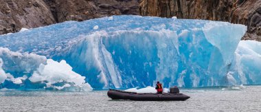 Fiyortta yüzen dev bir buzdağının yanından sürat teknesiyle geçen tek bir turist. Alaska, ABD