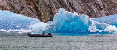 Fiyortta yüzen dev bir buzdağının yanından sürat teknesiyle geçen tek bir turist. Alaska, ABD