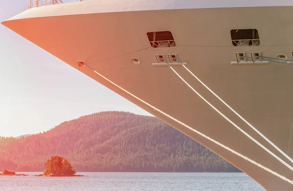 Ship's bow with sun glow. Ropes coming from the bow to the pier. Mountains and forest in the background.