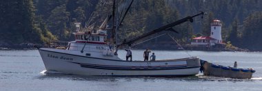 Sitka, Alaska, ABD - 10 Eylül 2018: Lisa Jean adlı balıkçı teknesi marinada denize açıldı. Arka planda hafif odaklı deniz feneri ve orman. Sitka, Alaska, ABD