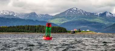 Alaska 'da arka planda dağlar olan bir deniz feneri ve şamandıra manzarası