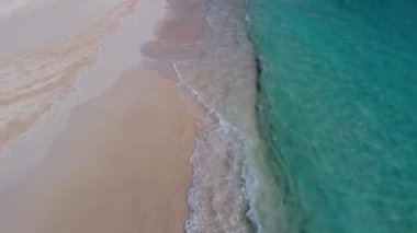 Dron 'un kumlu sahilde yüzeye çok yakın bir yerde süzülüşü. Aşağıda turkuaz ve köpüklü dalgalar var. Half Moon Cay Adası, Bahamalar..