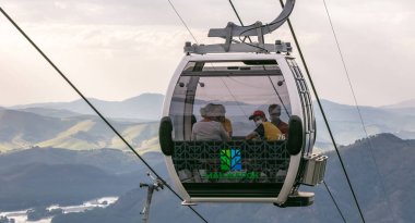 Manzherok tatil köyü, Altai Dağları, Rusya - 12 Ağustos 2020: İçinde maskeli turistlerle birlikte teleferik çekimleri. Bulutlu bir arka plan. Yeni Covid 19 gerçeklik kavramı.