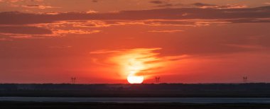 Gün batımında güzel panoramik manzara. Kırmızı ve turuncu gökyüzü. Güneş diskinin yanındaki yüksek voltajlı elektrik hatları. Altai Krai, Sibirya 'daki Rus kırsal bölgesi..