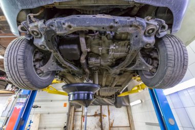 Rutin hizmet sırasında atölyedeki hidrolik asansörde arabadaki motor yağını boşaltmak. Düşük açılı çekim.