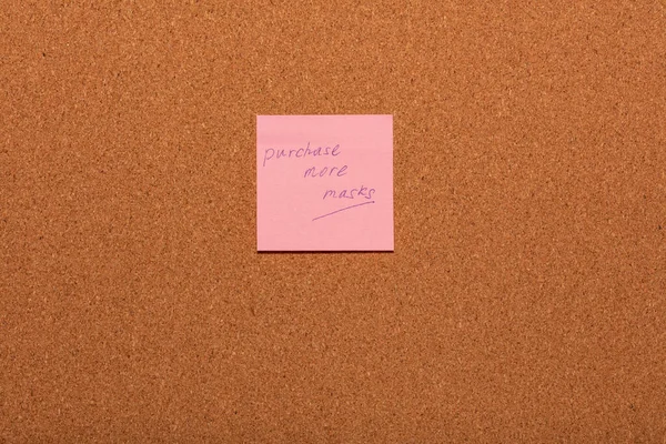 Reminder Purchase more masks handwritten on a pink sticker on a cork notice-board. Healthcare and social concepts.