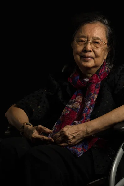 Asian elder woman in her wheelchair feeling lonely on black background