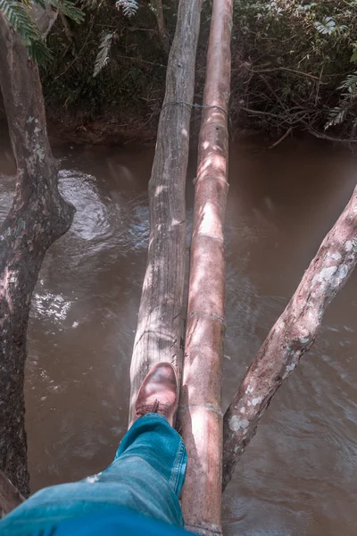 Vista aérea de pés de homem com sapatos marrons cruzando ponte de madeira sobre o rio de água turva — Fotografia de Stock