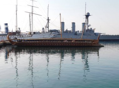 Eski bir savaş gemisinin tam ölçekli bir kopyası, Faliro, Attica, Yunanistan 'da eski bir kruvazör ve diğer eski gemilerin önünde.