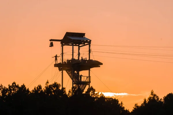 Torre a zipline con sagome di persone al tramonto — Foto Stock